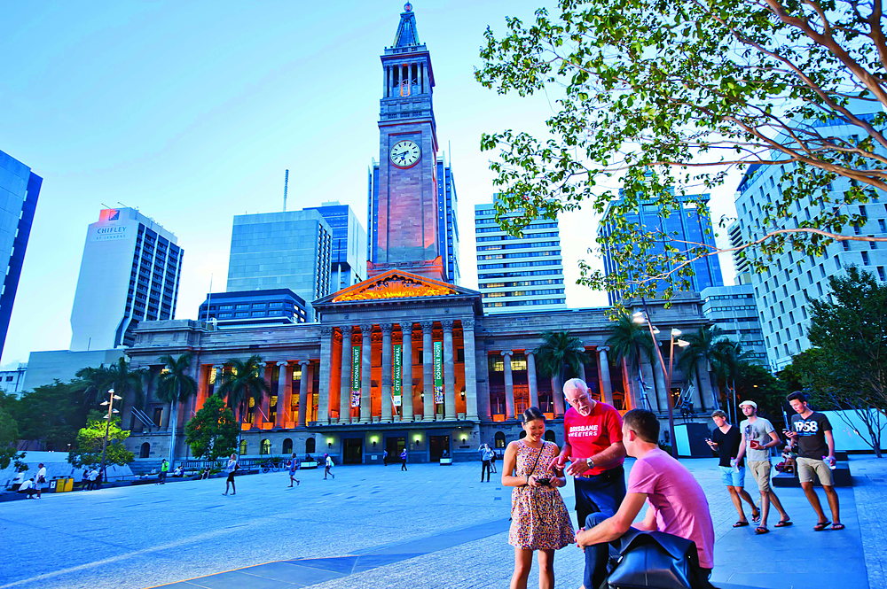 People walking across King George Square in front of Brisbane City Hall on a bright day